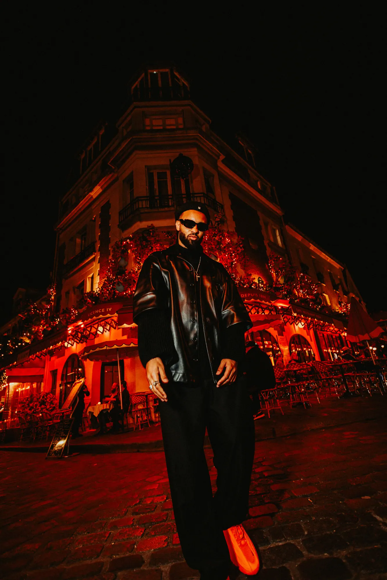 OKEMI in a black leather jacket in front of a Paris corner café lit in red